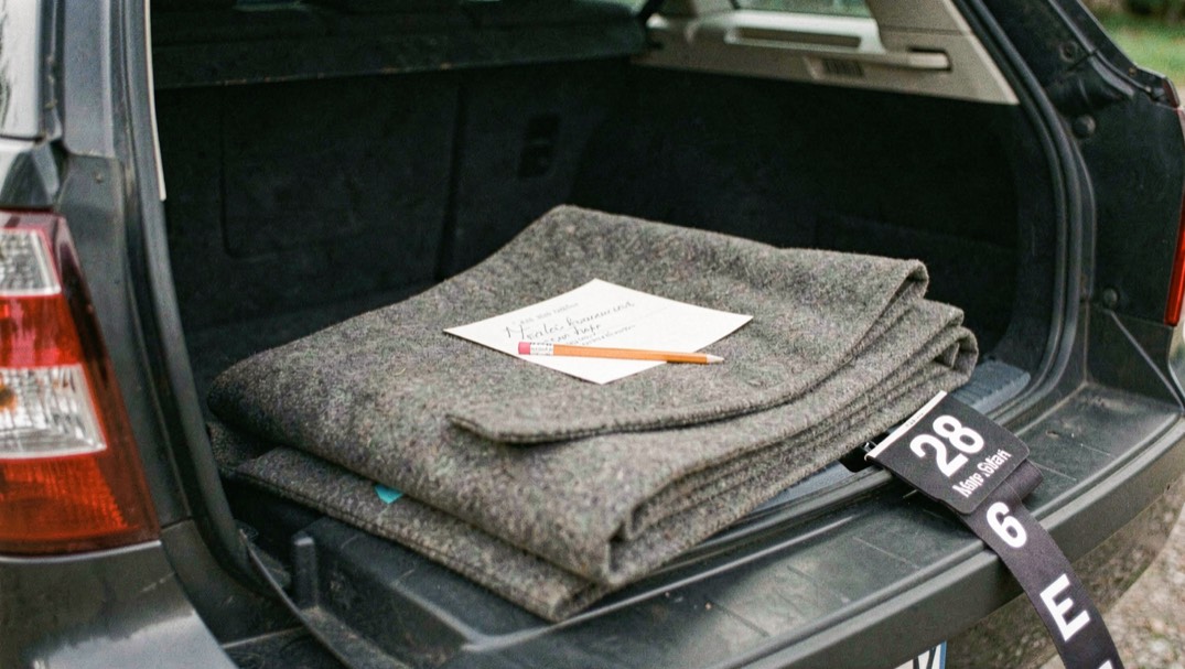 A judge’s marked card and pencil resting on a folded coat on the tailgate of an estate car, a numbered arm band beside it